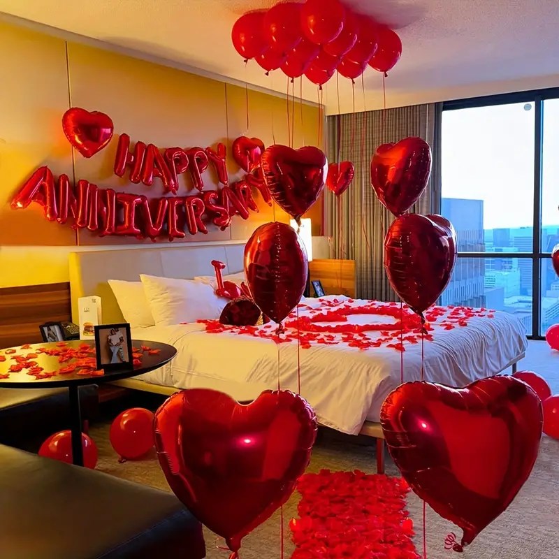 A beautifully decorated hotel room for an anniversary, featuring red balloons, heart shaped decor, and rose petals on the bed